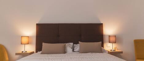 A neatly made bed with a headboard, two bedside lamps, and two chairs.