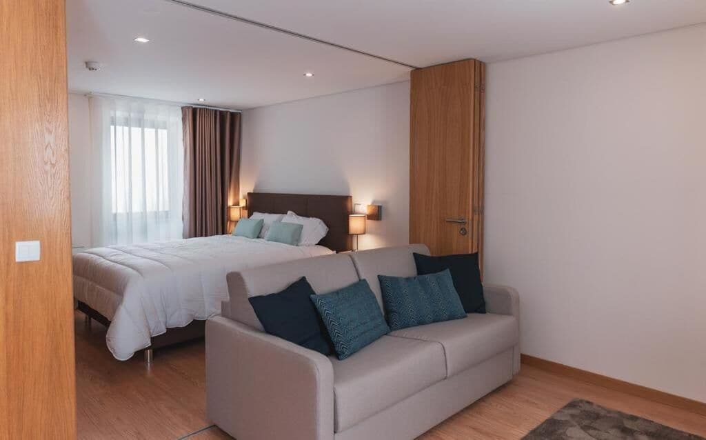 A modern hotel room with a bed, a sofa, and a wooden wardrobe.