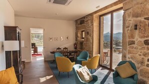 A spacious living area with a stone wall, a dining table with chairs, and a view of the mountains.