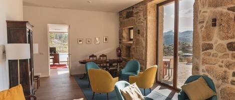Un amplio salón con pared de piedra, una mesa de comedor con sillas y vistas a las montañas.