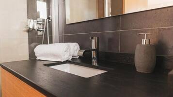 A modern bathroom with a dark countertop, a white sink, a mirror, and a towel.