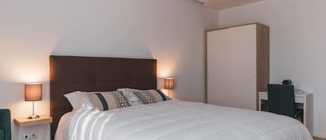 A modern bedroom with a large bed, two bedside lamps, a desk, and a wardrobe.