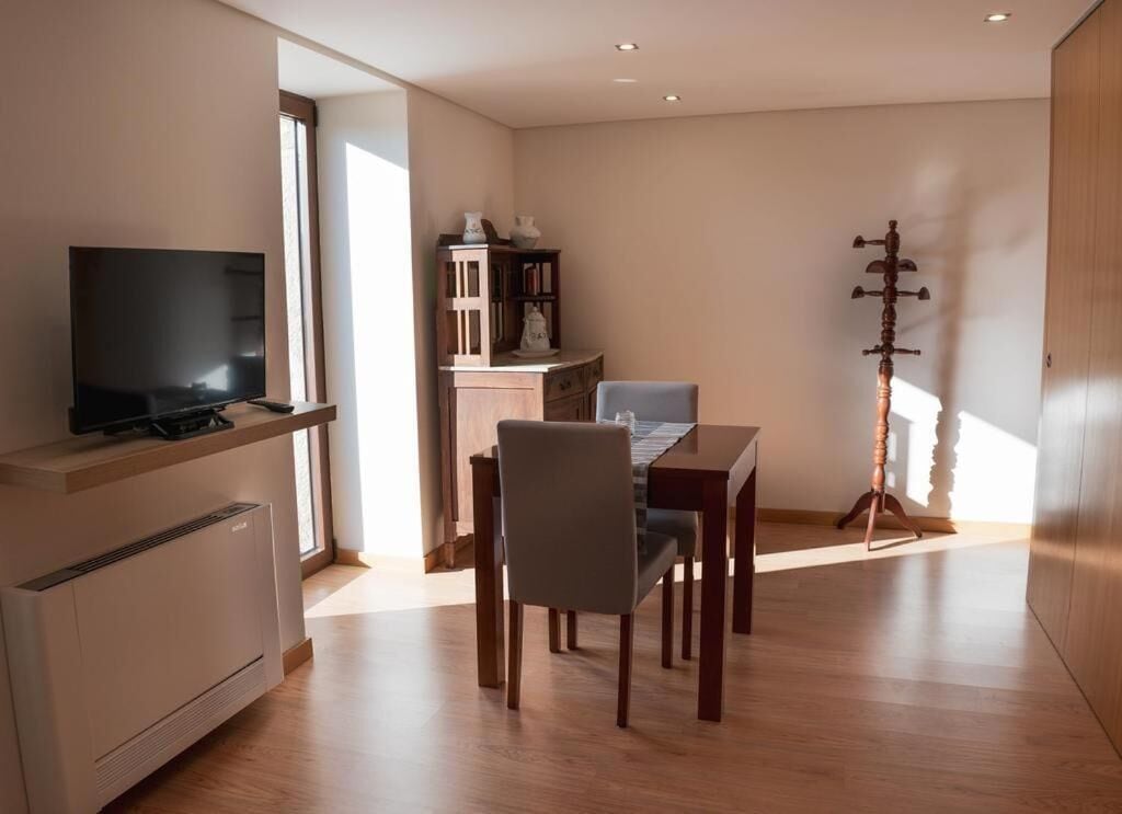 Ein modernes Wohnzimmer mit Flachbildfernseher, einem Esstisch mit Stühlen, einem Bücherregal und einer Dekorationsecke.