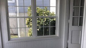 A room with a large window, a wicker chair, a small table with a vase of flowers, and a door. - Sandcastle park! Basketball, Tennis, beach, mini golf, ice cream & restaurants! (Ocean City)