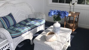 A white wicker sofa with a striped cushion, a small white table with a vase of blue flowers, and a wicker basket on a dark floor. - Sandcastle park! Basketball, Tennis, beach, mini golf, ice cream & restaurants! (Ocean City)