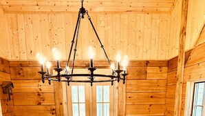 L’intérieur d’un chalet en bois, avec un escalier central, un lustre et une fenêtre offrant une vue dégagée.