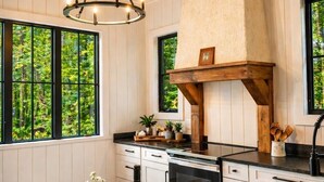 Une cuisine avec des poutres apparentes en bois au plafond, un îlot central et de grandes fenêtres donnant sur un paysage verdoyant.