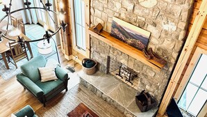 Un salon spacieux avec une cheminée en pierre, un canapé vert, une table basse en bois et un luminaire suspendu.