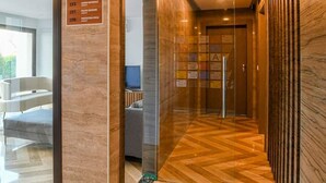 Un couloir avec un plancher en bois, une enseigne indiquant le « Club House », et une porte donnant sur une pièce où se trouvent un lit et un téléviseur.