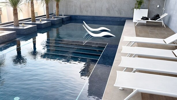 Une piscine intérieure moderne, avec de l’eau cristalline, des chaises longues blanches et des palmiers.