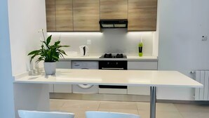 Une cuisine moderne avec un plan de travail blanc, deux tabourets de bar blancs, un four encastré et une plante en pot.