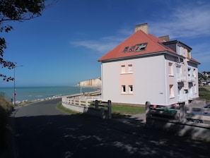 A coastal building with a red roof, a balcony, and a view of the sea.