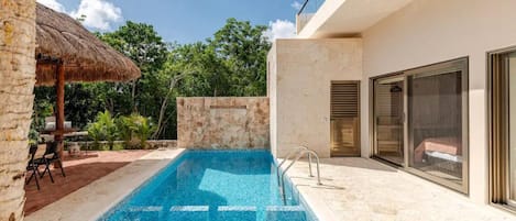 A modern outdoor swimming pool with a stone wall and a thatched-roof structure.