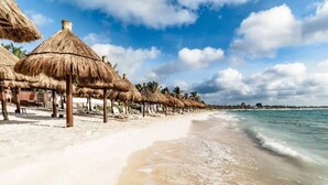 Een strand met rieten parasols en ligbedden, een zandstrand en een kalme zee.