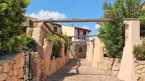 Un sentier pavé de pierres mène à un bâtiment doté d’une arche en pierre et d’une pergola en bois.