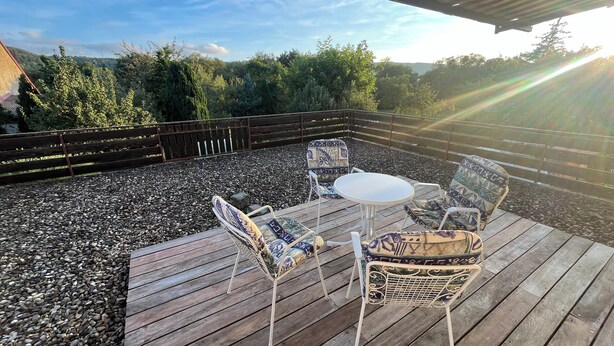 Une terrasse extérieure dotée d’une plateforme en bois, entourée d’une clôture en bois, et comprenant une table et quatre chaises avec des coussins à motifs.