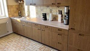 Une cuisine avec des armoires en bois, un plan de travail et un évier. On peut voir divers ustensiles de cuisine sur le plan de travail, notamment une machine à café et un bloc à couteaux.