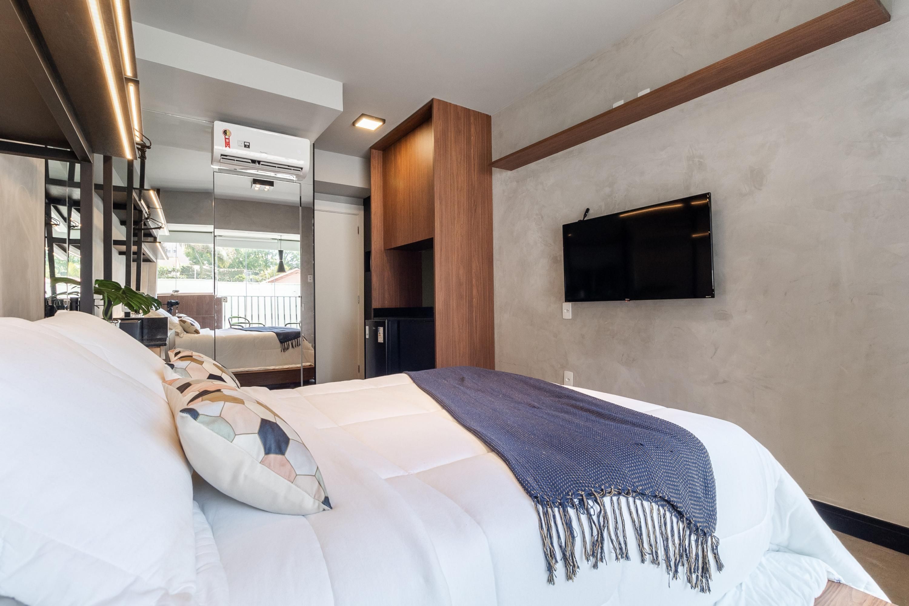 Una camera d'albergo moderna con un letto grande, una TV a parete e aria condizionata integrata.