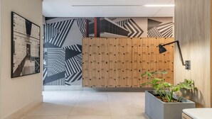 A modern lobby with lockers, a large abstract mural, and a potted plant. - Seng 106 in S o Paulo (São Paulo)