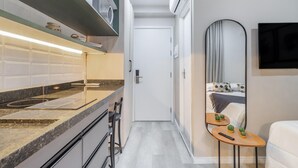 A modern kitchen with a built-in oven, a microwave, and a stainless steel sink. There is a small wooden table with a remote control and a mirror on the wall. - Seng 106 in S o Paulo (São Paulo)