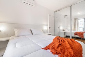 A modern hotel room with a large bed, a glass partition wall, and a view of the city.