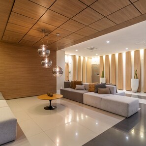 A modern lobby with a wooden ceiling, a sectional sofa, a round coffee table, and a large potted plant.