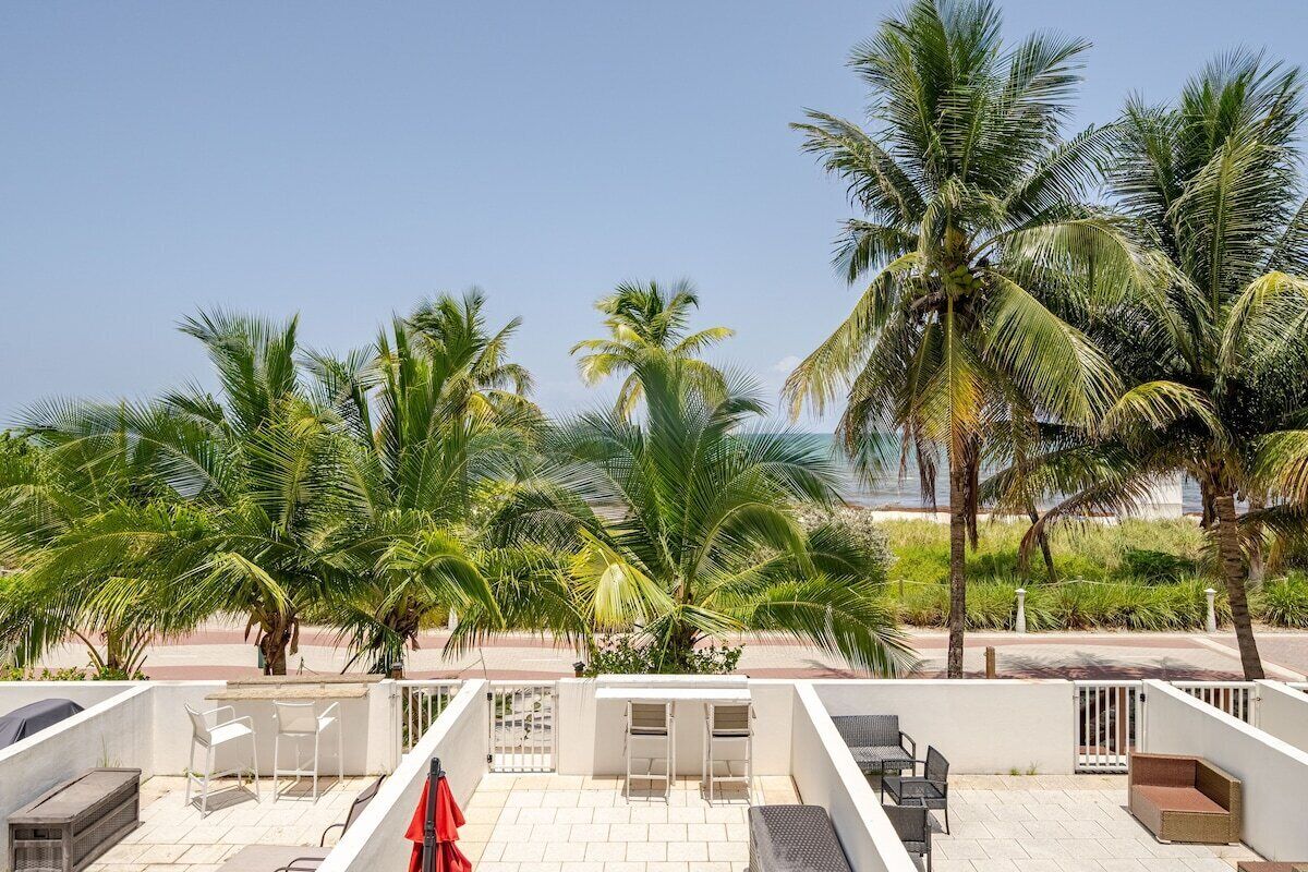 A rooftop terrace with outdoor seating, palm trees, and a clear view of the ocean.