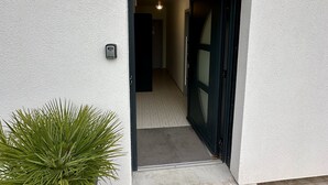 Ingresso di un edificio con pavimento piastrellato, una pianta in vaso e una porta che conduce a un ambiente interno.