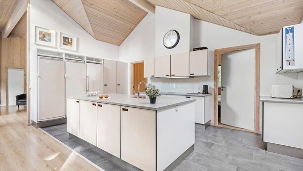 A modern kitchen with a central island, wooden ceiling, and white cabinetry.
