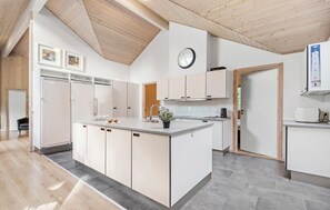 A modern kitchen with a central island, wooden ceiling, and white cabinetry. - Lovely home in Blåvand with kitchen (Blåvand)