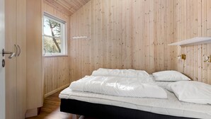 A bedroom with a wooden paneled wall, a bed with white bedding, a window, and a door with a handle.