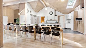 A modern kitchen with white cabinets, a wooden ceiling, and a dining area with black chairs and a wooden table.