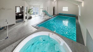 An indoor swimming pool with a slide, a hot tub, and a view of the outside.
