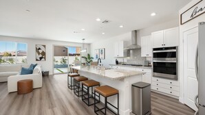 Uma cozinha moderna com armários brancos, eletrodomésticos de aço inoxidável e uma ilha central com banquetas.
