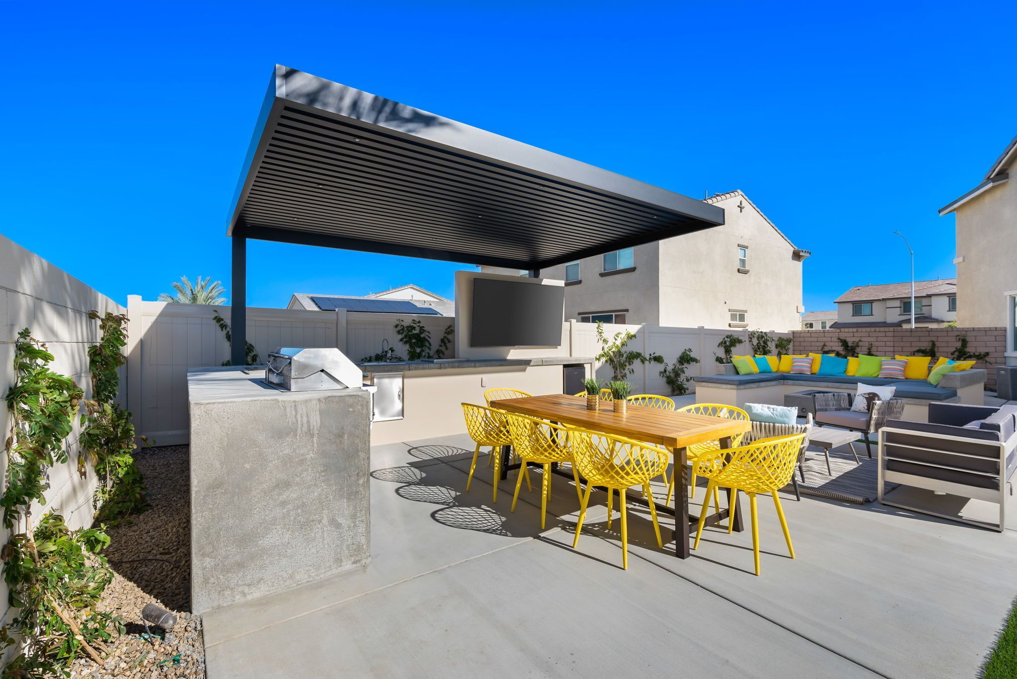 Une terrasse extérieure avec une table en béton et des chaises jaunes, un barbecue et un espace salon abrité.