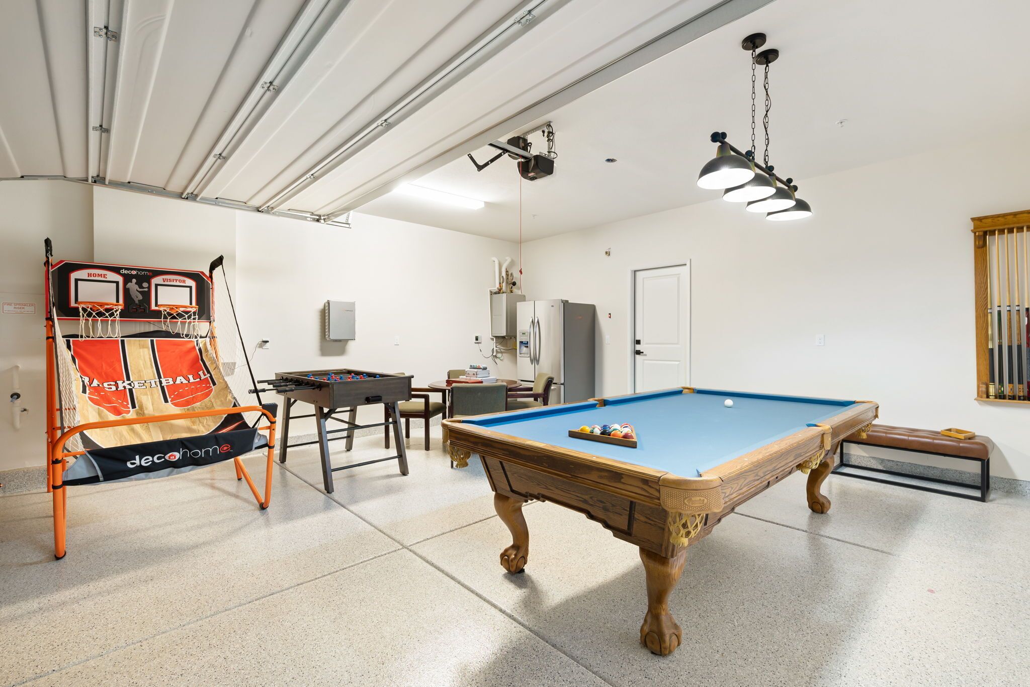 A room with a pool table, a basketball hoop, and a refrigerator.