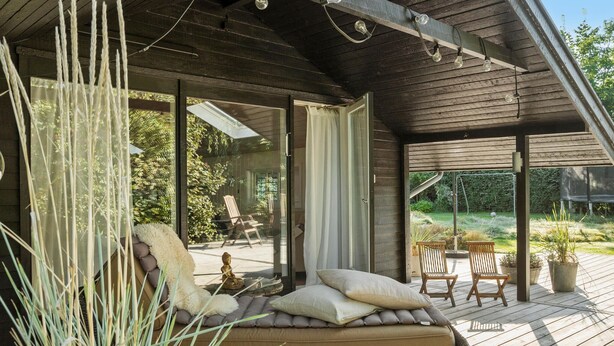 A covered outdoor seating area with a sofa, cushions, and a Buddha statue.
