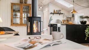 A cozy kitchen with a central wood-burning stove, a dining area with a table set for two, and a kitchen counter with various items.