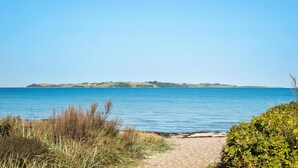 A coastal path leading to a beach with clear blue water and distant hills.