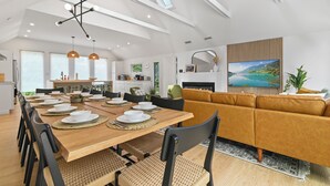 Ein modernes Wohnzimmer mit einem Holzesstisch, der für sechs Personen gedeckt ist, einer Couch und einem Kamin.
