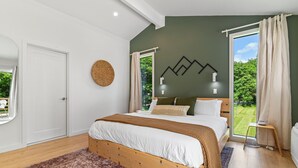 Ein Schlafzimmer mit einem hölzernen Bett, Blick ins Grüne und einem modernen Wanddesign.