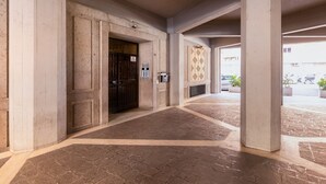 Um corredor com porta, colunas e ladrilhos no chão com padrão.