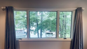 Een kamer met een groot raam dat uitkijkt op water en bomen.