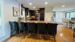 Een moderne keuken met een centraal eiland, donkere houten keukenkasten en een eethoek met zes stoelen.