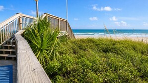 Ein hölzerner Steg führt zu einem Strand bei strahlend blauem Himmel.