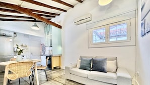 Un salon moderne avec un canapé, un coin repas comprenant une table et des chaises, et une cuisine en arrière-plan.