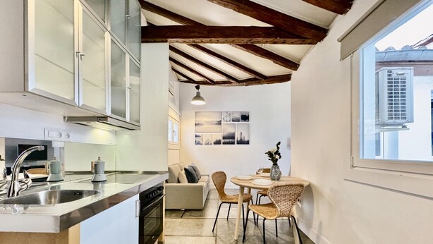 Une cuisine moderne dotée d’un îlot central, d’un coin repas avec des chaises en osier et d’une grande fenêtre offrant une vue sur l’extérieur.