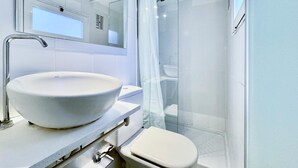Une salle de bain moderne dotée d’un grand lavabo sur pied, de toilettes et d’une douche à parois de verre.