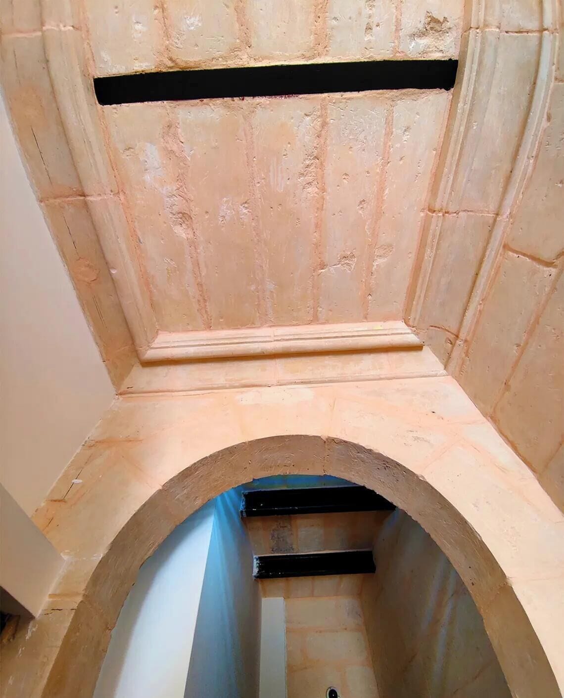 Ein Raum mit einer gewölbten Decke, einer hölzernen Bank und einem Durchgang zu einem weiteren Bereich.