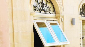 A building facade with a yellow exterior, a window with a metal frame, and a door with a decorative design. - Savynomad Harbour Residences Bormla (Cospicua)